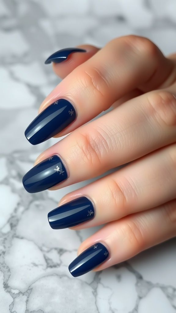 A close-up of dark blue nails with silver foil accents on a marble surface.