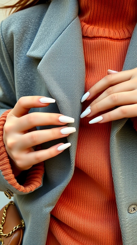 Close-up of hands with white chrome nails, wearing a gray coat and orange sweater.